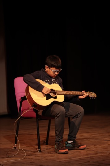 Child playing an acoustic guitar solo on stage at WKC Showcases